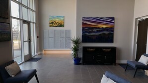 Un hall d’entrée avec deux fauteuils bleus, une plante en pot, un tableau représentant un coucher de soleil, une rangée de casiers et une grande fenêtre.