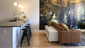 Une cuisine moderne dotée d’un îlot central, de tabourets de bar, de luminaires suspendus et d’une grande fresque représentant une scène historique.