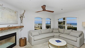 A living room with a large L-shaped sectional sofa, a round coffee table, and a fireplace. There are three large windows providing a view of the ocean. - Gorgeous Overlooking Gulf,Patio, Pool, Grill (Santa Rosa Beach)