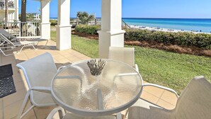 A covered outdoor seating area with a glass table and chairs, overlooking a beach. - Gorgeous Overlooking Gulf,Patio, Pool, Grill (Santa Rosa Beach)