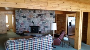 A cozy living room with a stone fireplace, a plaid sofa, and a wooden ceiling. - Beautiful Burt Lake sunsets and sandy beach (Indian River)