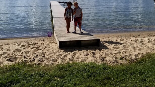 A wooden pier extending into a calm lake with a clear sky and scattered clouds. - Beautiful Burt Lake sunsets and sandy beach (Indian River)