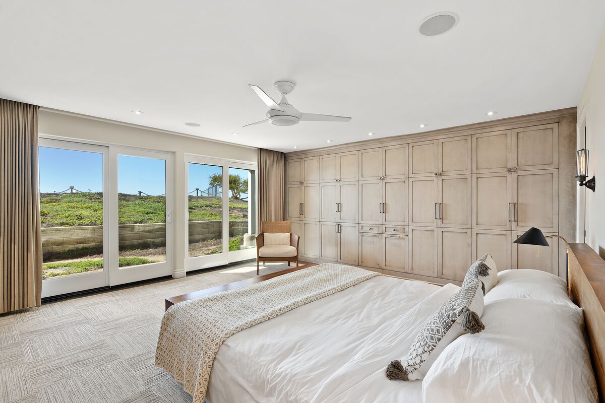 A spacious bedroom with a large bed, a ceiling fan, and a view of a green landscape through large sliding doors.