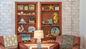 Un salon avec deux fauteuils en cuir, une bibliothèque en bois ornée d’objets décoratifs et une lampe posée sur une table en verre.