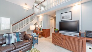 Un salon spacieux avec un canapé en cuir marron, un meuble de rangement en bois intégrant un téléviseur à écran plat, un escalier et un tableau encadré au mur.