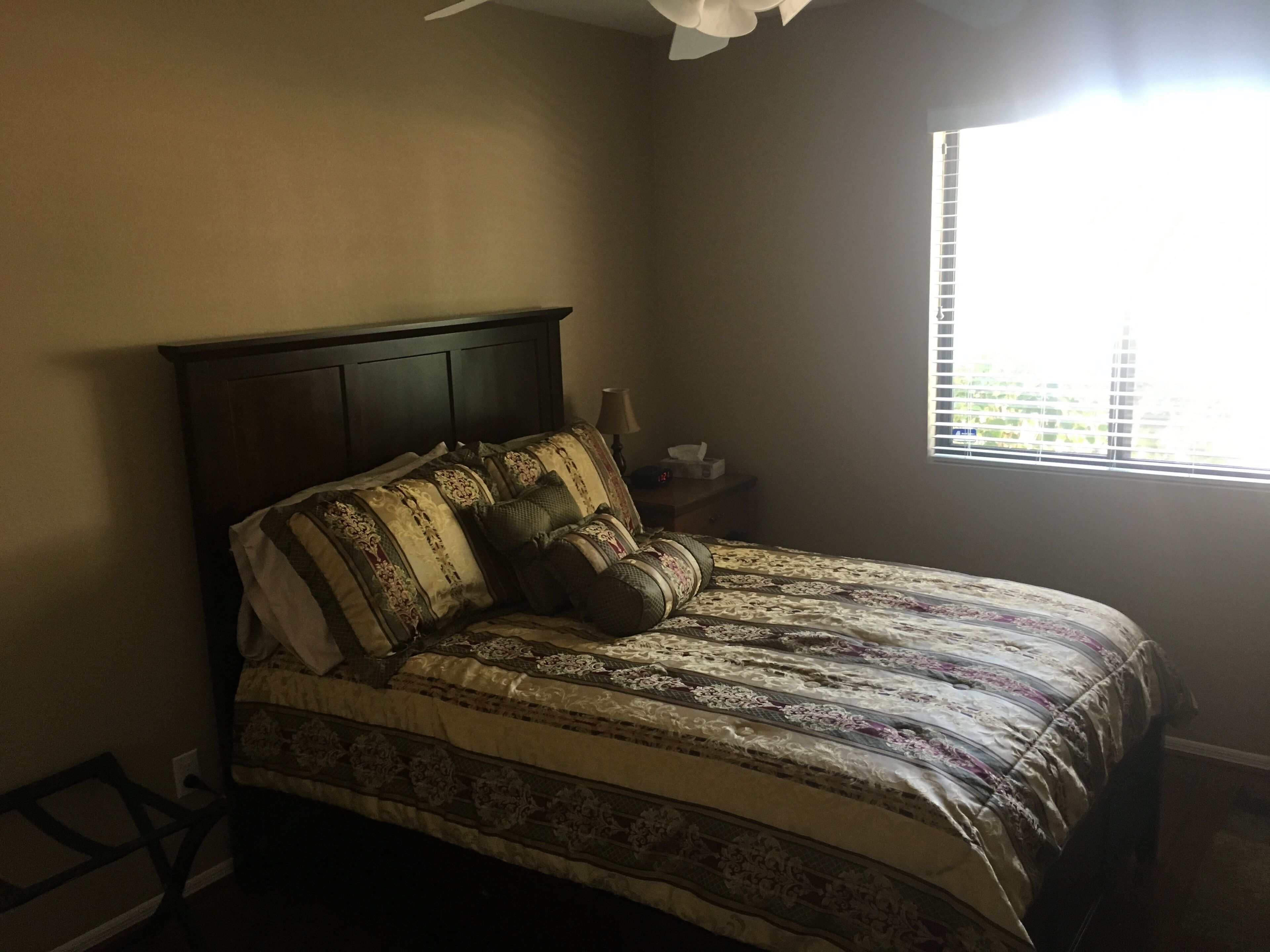 A bedroom with a bed, a nightstand, a lamp, and a window with blinds.