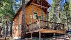 A log cabin with a wooden deck and multiple windows, surrounded by tall trees. - (12) Cabin Twelve at The Redwoods In Yosemite (Wawona)