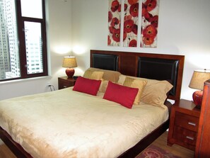 A neatly made bed with red and beige pillows, a wooden headboard, and a nightstand with a lamp. - Extra Large 2-bdrm, 2 bath at Harbor Steps - Walk to Pike Place, Waterfront! (Seattle)