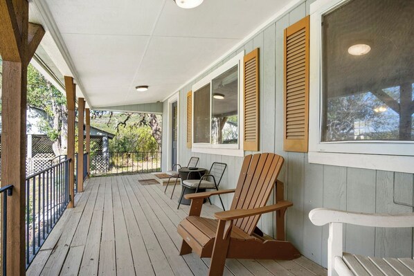 A covered porch with wooden railings, two Adirondack chairs, and a table.