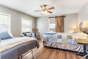 A bedroom with two beds, a ceiling fan, a wooden door, and a window with blinds.