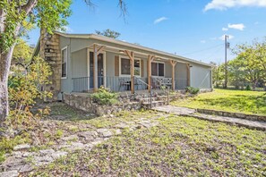A single-story house with a porch, stone foundation, and a grassy yard.