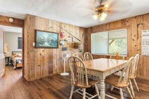 A dining area with a wooden table and chairs, a ceiling fan, and a window with a view.