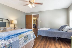 A bedroom with two beds, a ceiling fan, a nightstand with a lamp, and a door leading to another room.