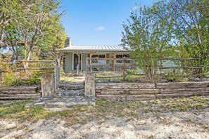 A rustic building with a porch, surrounded by a wooden fence and vegetation.
