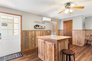 A kitchen with wooden paneling, a bar counter, a ceiling fan, and a wall-mounted air conditioner.