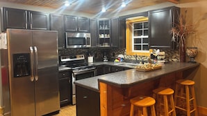 Une cuisine moderne dotée d’appareils électroménagers en acier inoxydable, de meubles de rangement en bois foncé, d’un grand îlot central avec des tabourets et d’une fenêtre offrant une belle vue.