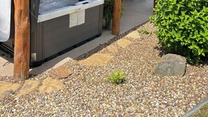 Un espace extérieur abrité comprenant un jacuzzi, une terrasse en bois et un bâtiment avec un toit rouge.