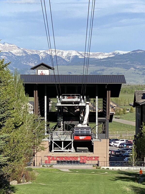Ein Berggasthof mit Seilbahn, Parkplatz und Blick auf verschneite Berge.