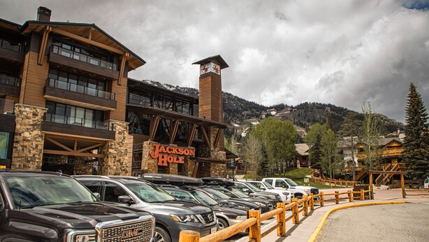Un hotel con una torre del reloj destacada, varios pisos y una fila de SUVs estacionados.