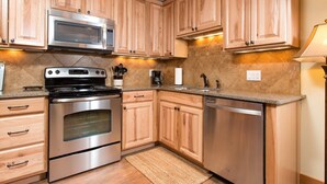Una cocina con armarios de madera, electrodomésticos de acero inoxidable, microondas, estufa, horno, lavavajillas y encimera de granito, además de una alfombra pequeña.