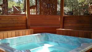 Ein Whirlpool mit Holzliegen auf einer Holzterrasse, umgeben von einem Holzzaun und Bäumen.