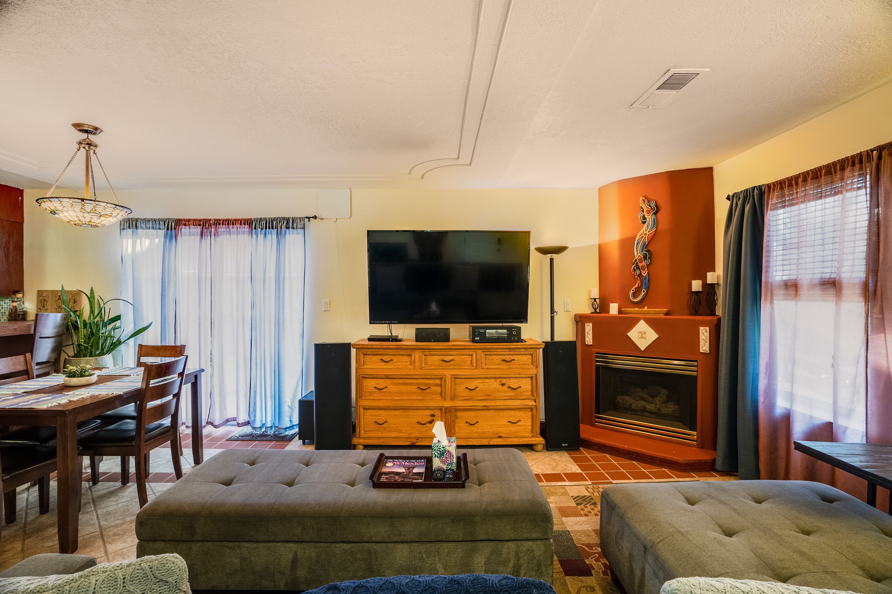A living room with a television, wooden cabinet, fireplace, and a dining area with chairs and a table.