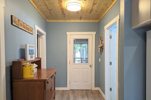 A hallway with a wooden ceiling, a white door with a glass panel, and a shelf with a yellow container.