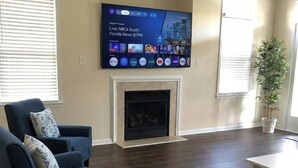 A living room with a flat-screen TV mounted on the wall, a fireplace, and a potted plant.