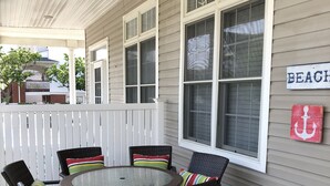 A covered patio with wicker furniture and a round table, a white fence, and a 'BEACH' sign on the wall.