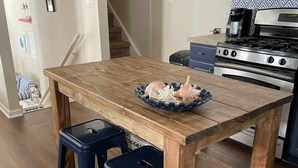 A kitchen with a wooden table, two blue stools, a stove, and a coffee maker.