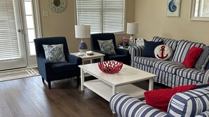 A living room with a dark blue armchair, a striped sofa, a white coffee table, and a wicker chair.