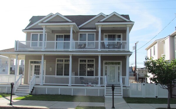 Stunning two-story home with a central entrance, white railings, and a well-manicured lawn.