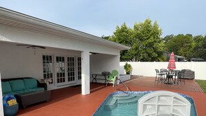 Un patio trasero con piscina, un área de porche techado y mobiliario exterior.