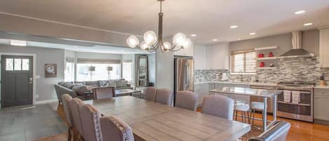 A modern kitchen with a central island, a dining area with a large table and chairs, and a living room with a sofa and coffee table.
