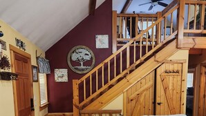 A cozy living room with a wooden staircase, a sofa with floral cushions, and a wooden coffee table. - 3BR/2BA. Mtn Cabin- Cool, Rocky Mtn. Stream. Prime Fall weeks available (Cashiers)
