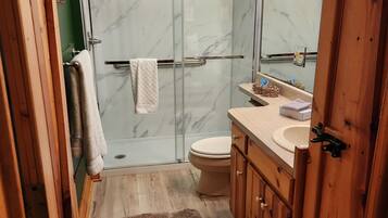 A bathroom with a glass shower enclosure, a toilet, a sink, and wooden cabinets.