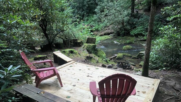 A wooden deck with two Adirondack chairs overlooking a natural stream. - 3BR/2BA. Mtn Cabin- Cool, Rocky Mtn. Stream. Prime Fall weeks available (Cashiers)