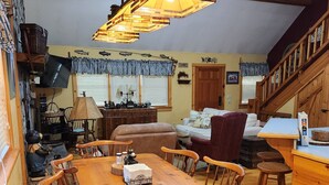 A cozy dining area with a wooden table and chairs, a hanging light fixture, and a staircase leading to another level. - 3BR/2BA. Mtn Cabin- Cool, Rocky Mtn. Stream. Prime Fall weeks available (Cashiers)