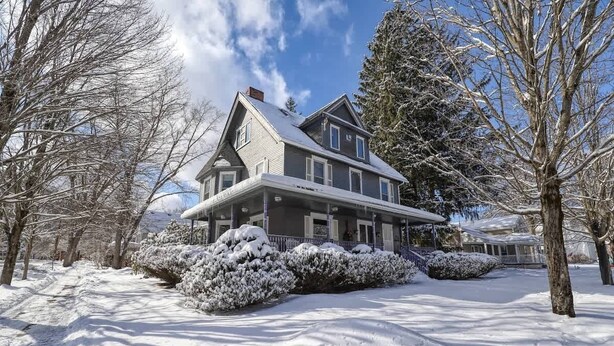 A large, two-story house with a covered porch and snow-covered landscape.