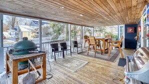 A covered outdoor area with a wooden deck, a grill, and a dining table with chairs.