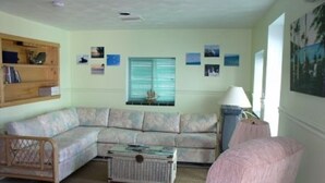 Ein Wohnzimmer mit einem Ecksofa, einem kleinen Tisch, einem Sessel und einem Fenster mit Jalousien.