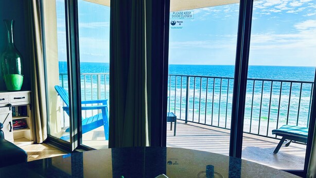 A view from a room with a large window overlooking the ocean, a dining area with a table and chairs, and a sign indicating the door should be kept closed. - LAVISH OCEAN OASIS! DIRECTLY on the GULF, POWDERED SAND - ABUNDANT AMENITIES! (Orange Beach)