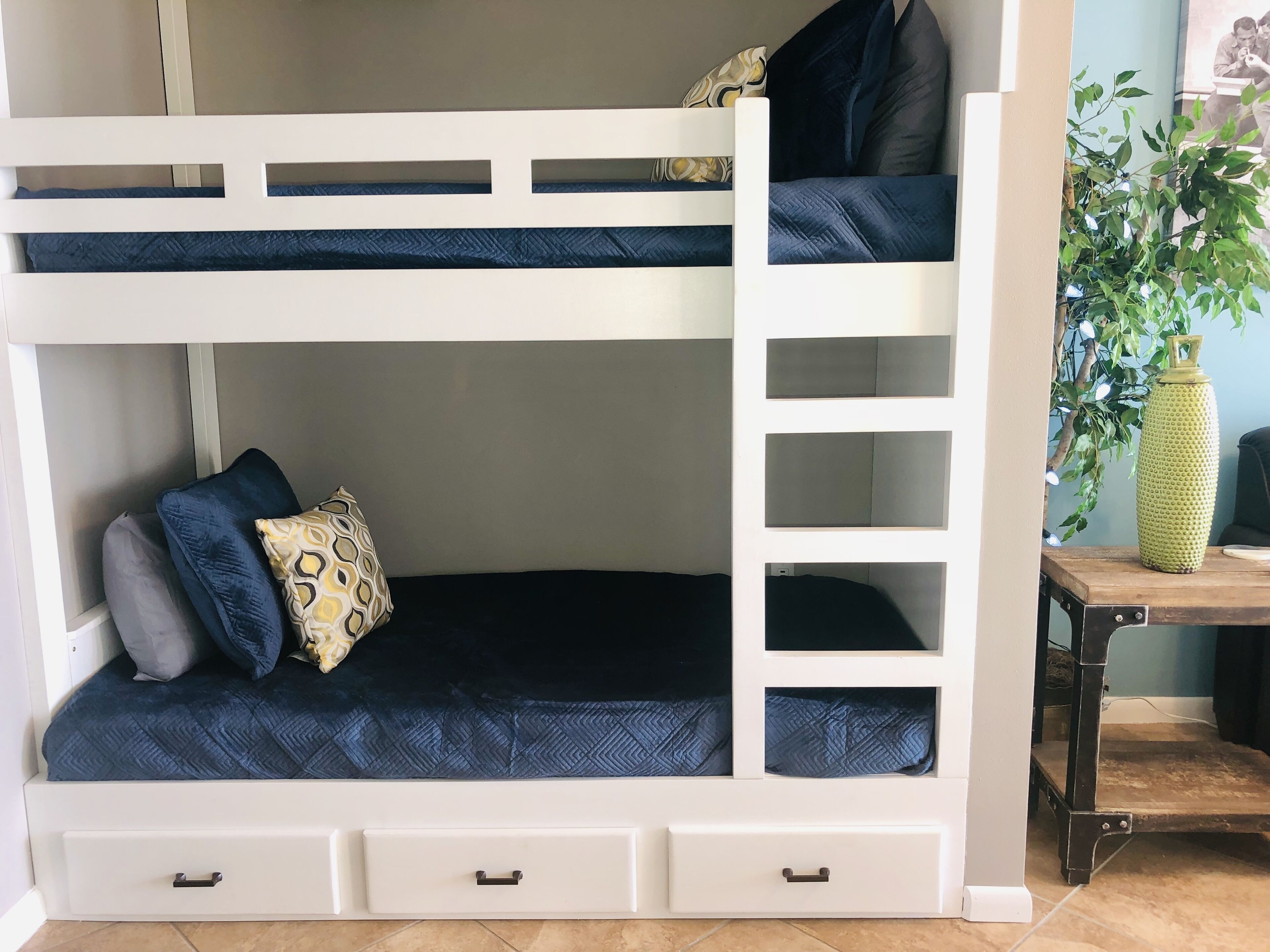 A bunk bed with a ladder, two drawers, and a small table with a plant.