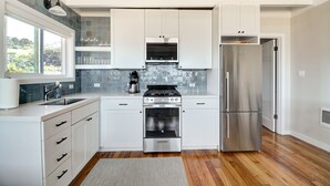 A modern kitchen with white cabinets, stainless steel appliances, and a large window offering a view of greenery.