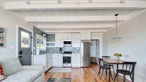 A modern kitchen with white cabinets, a stainless steel refrigerator, and a dining area with a wooden table and black chairs.