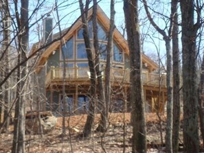 Surrounded by a forest, this cabin features a spacious balcony and large windows, with a chimney visible from the exterior.