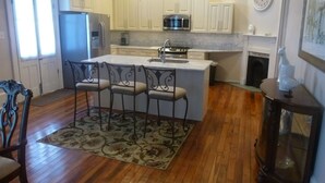 A kitchen with white cabinets, a central island with bar stools, a chandelier, and a fireplace.