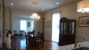 A spacious kitchen with a marble countertop and a sink, wooden dining table with chairs, a chandelier, and a cabinet with glass doors.