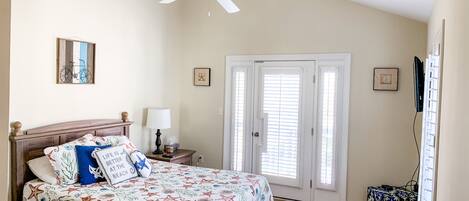 A bedroom with a bed, a ceiling fan, a nightstand, a lamp, a door with blinds, and a small table with a decorative item.