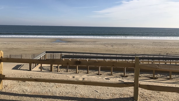 Une plage bordée d’une clôture en bois, offrant une vue dégagée sur l’océan.